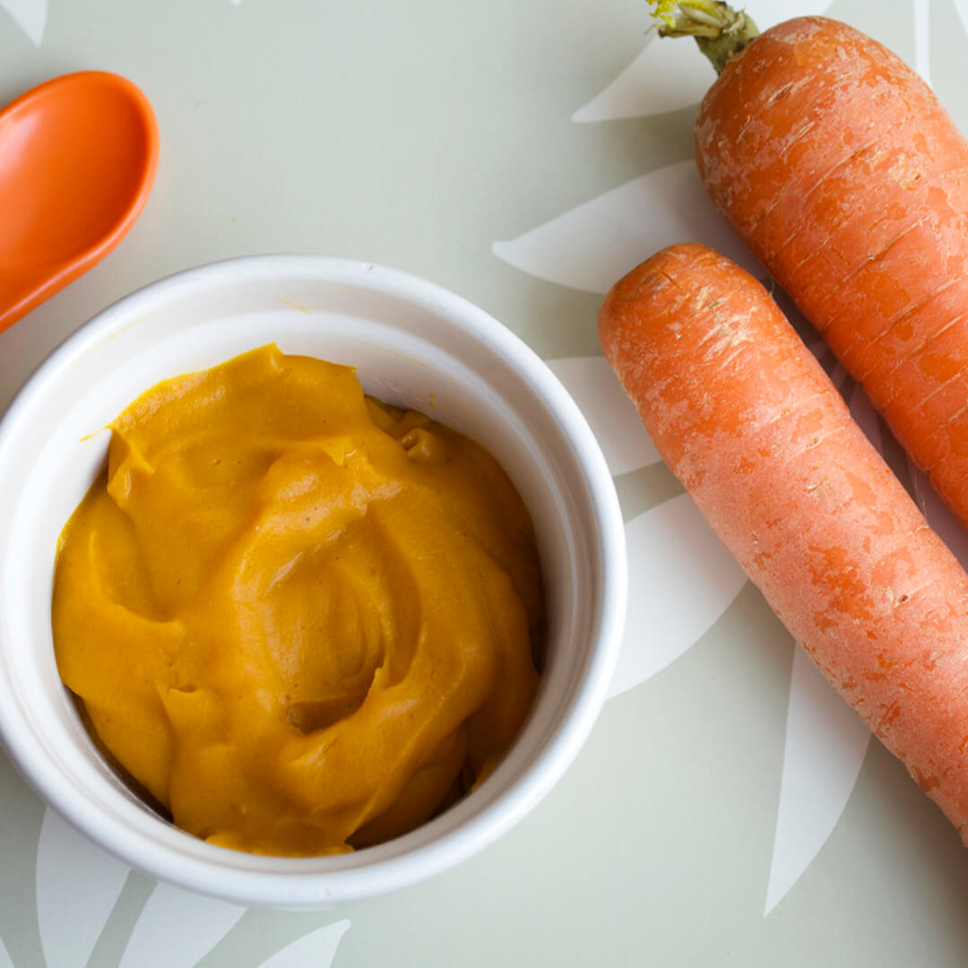 A small bowl of carrot puree next to two carrots