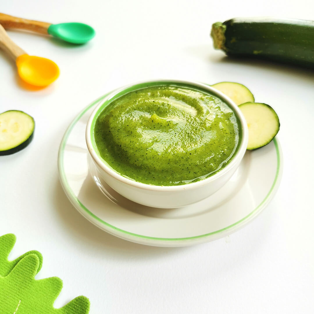 Courgette puree in a small bowl next to a whole courgette and some slice courgette