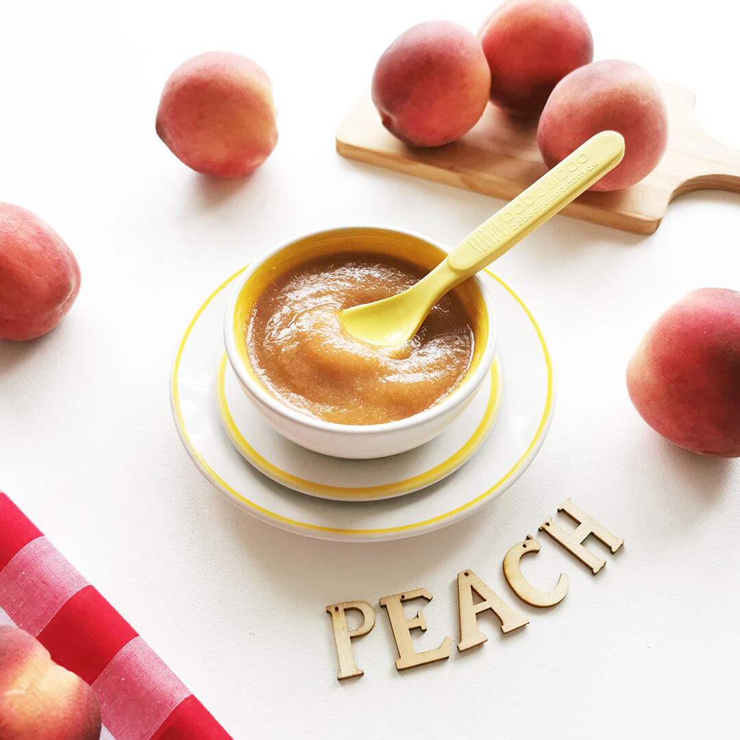 Peach puree in a bowl with some peaches around it