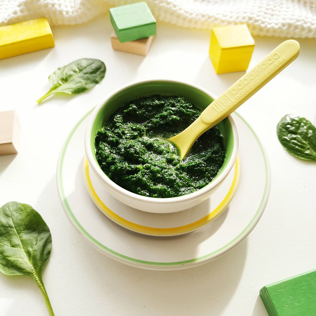 Spinach puree in a small bowl with some spinach leaves around it