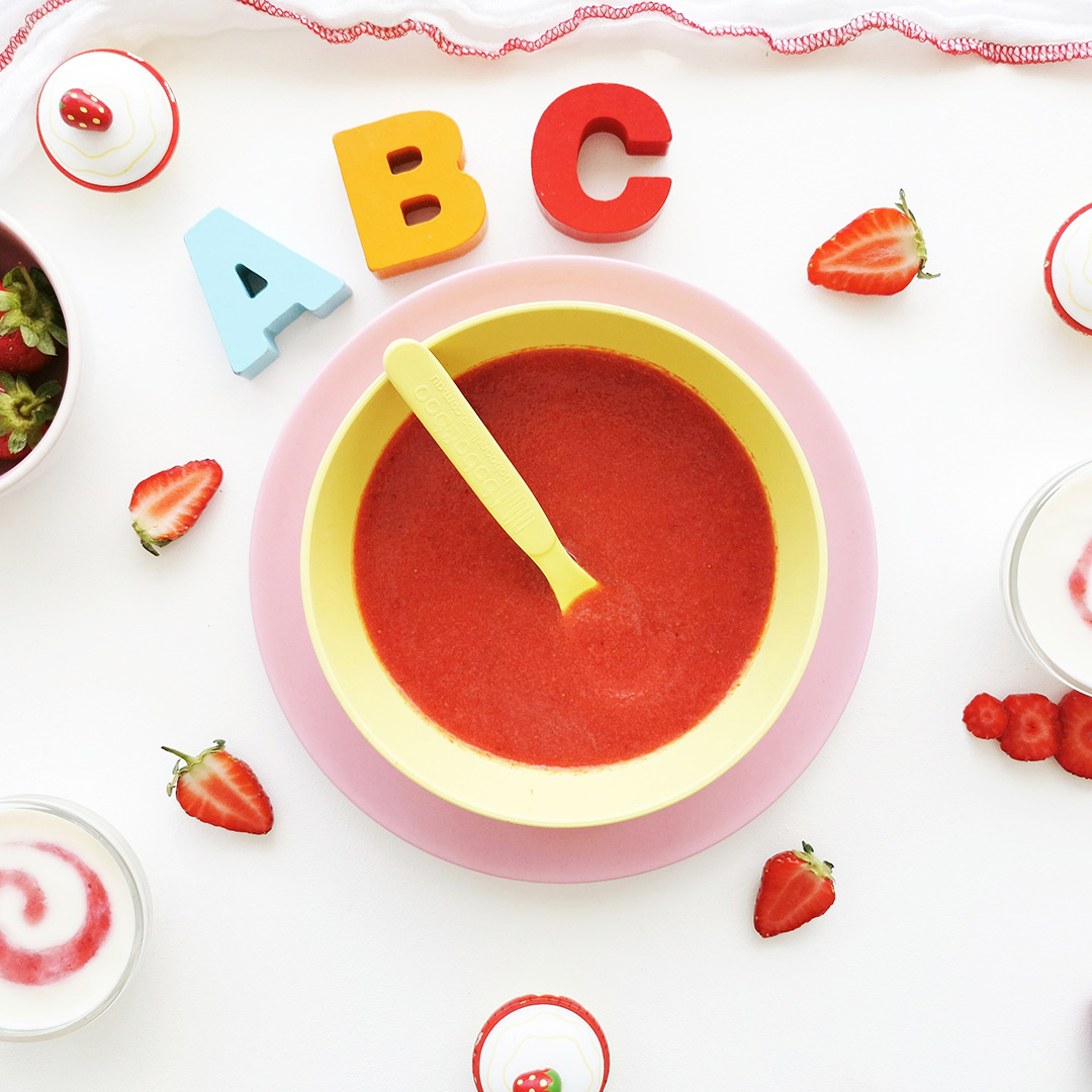 Strawberry puree in a small bowl with some sliced strawberries around it