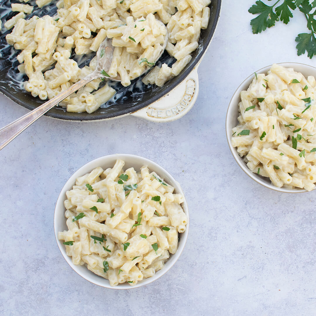 Two servings of Vegan Mac & Cheese next to a casserole dish of Vegan Mac & Cheese