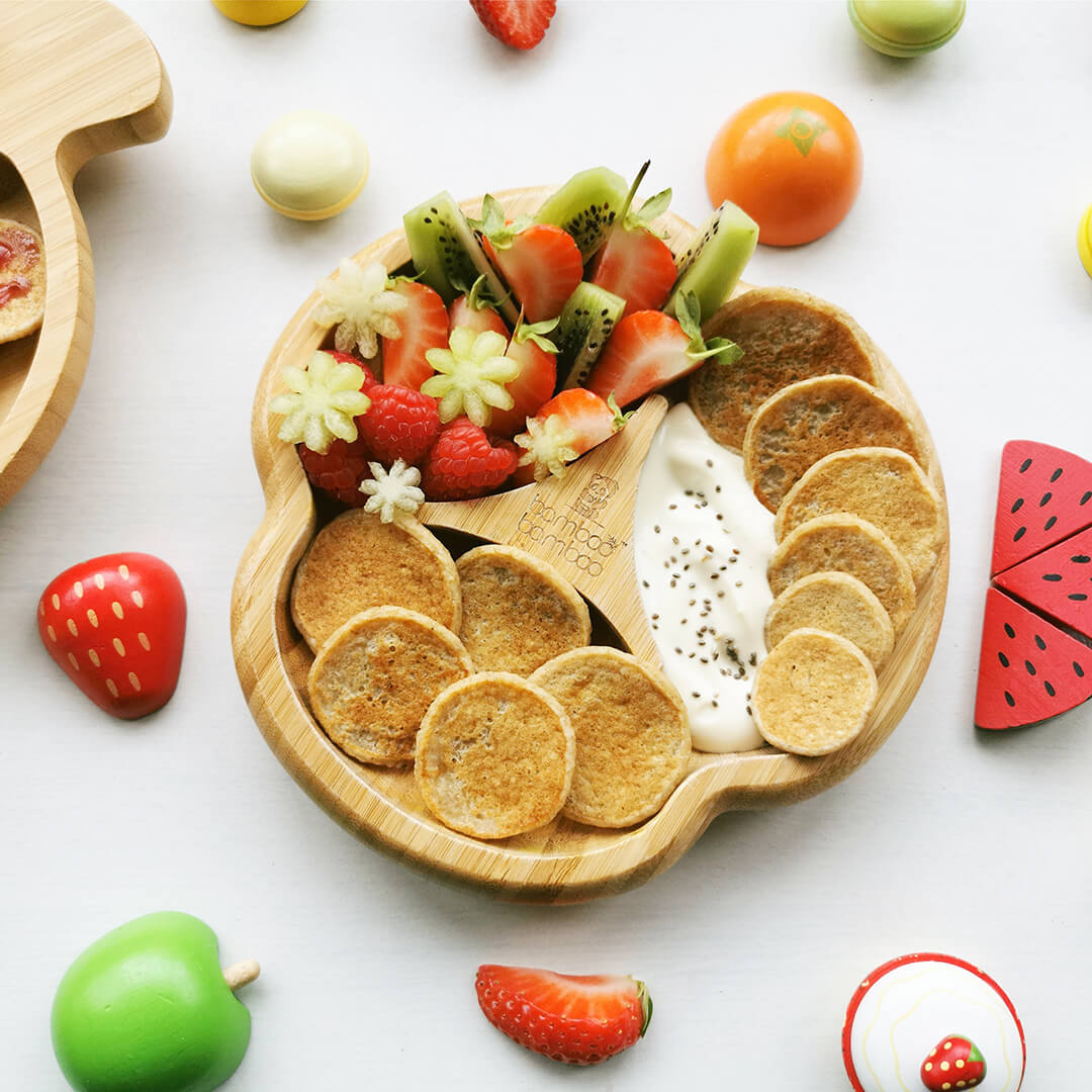 A serving if mini pancakes served with kiwi fruit, strawberries and yoghurt