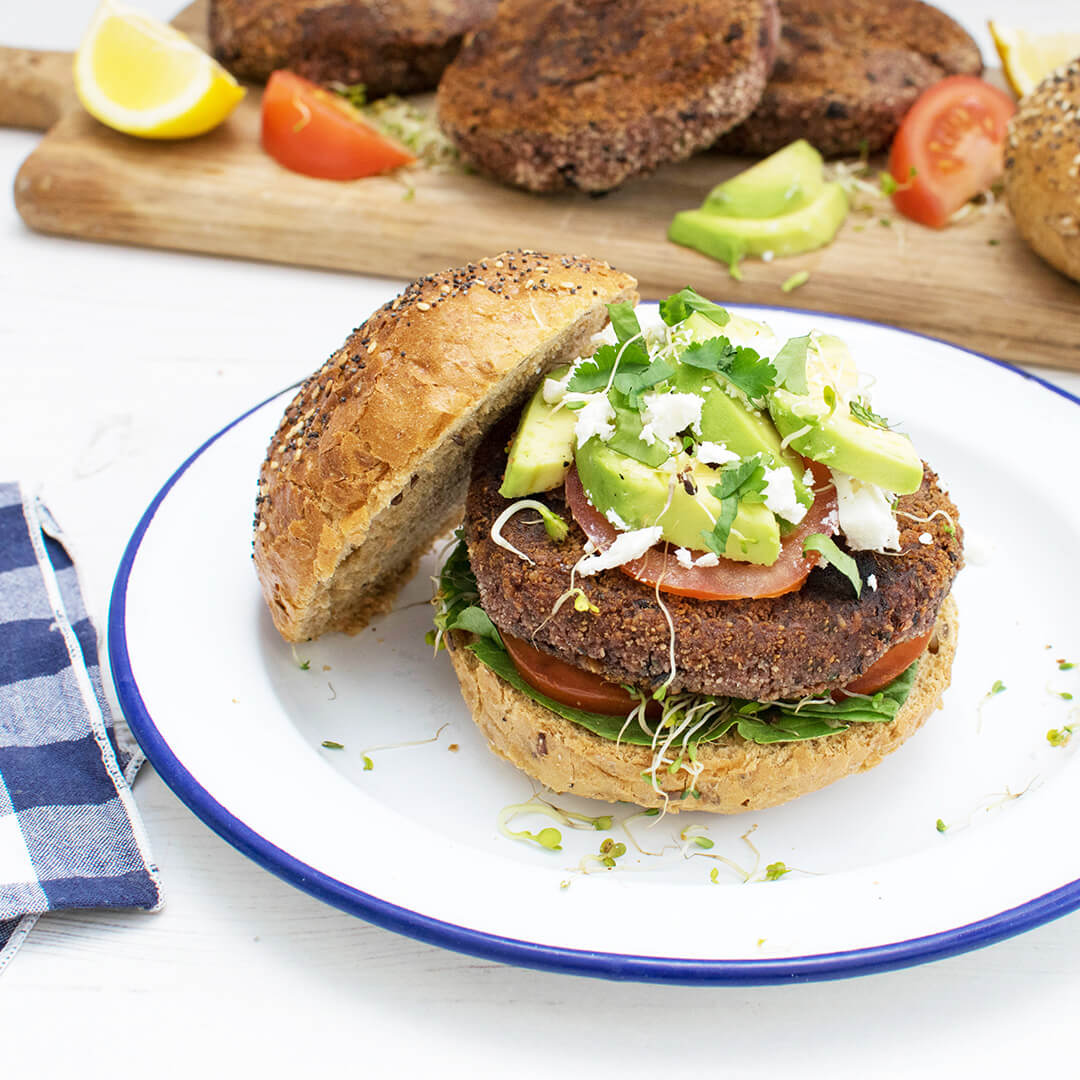 Beetroot burger in a seeded bun served with salad leaves, tomatoes, avocado and feta