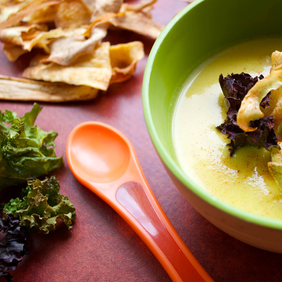 A bowl of Ginger & Butternut Soup next to some vegetable and kale crisps