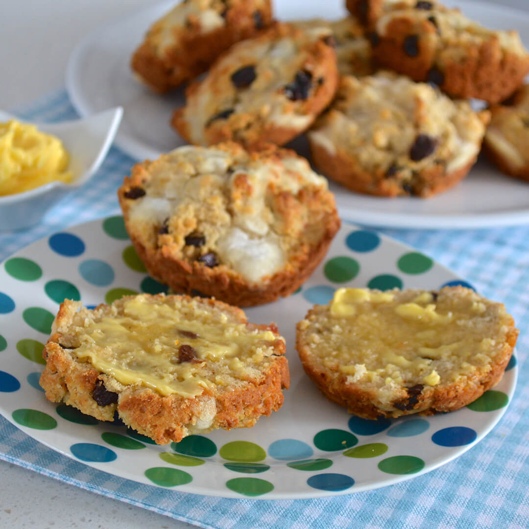 A plate of 3 hot cross muffins next to a plate of more hot cross muffins