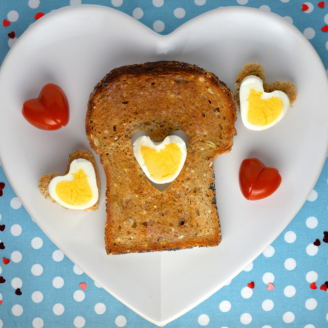 Toast with a heart shaped cut-out filled with a heart shaped boiled egg, served with 2 heart shaped boiled eggs and heart shaped tomatoes