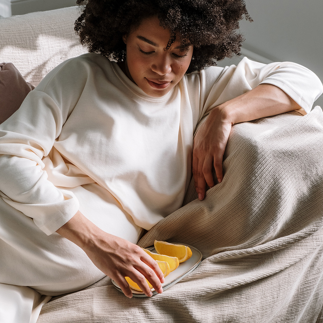 A woman sitting on a sofa with a plate of sliced orange