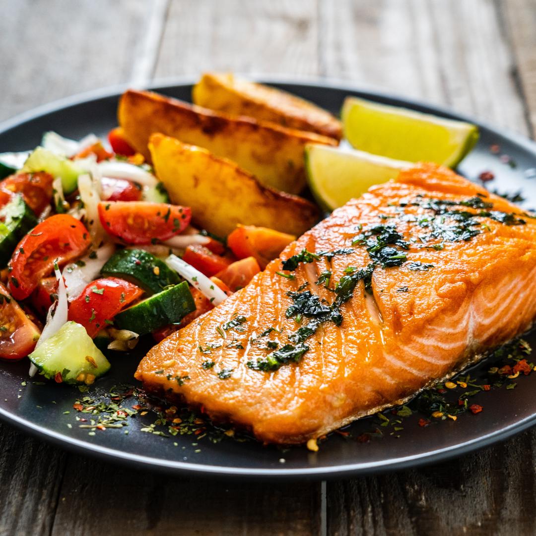 Plate with salmon fillet, vegetables, potato wedges and lemon wedges