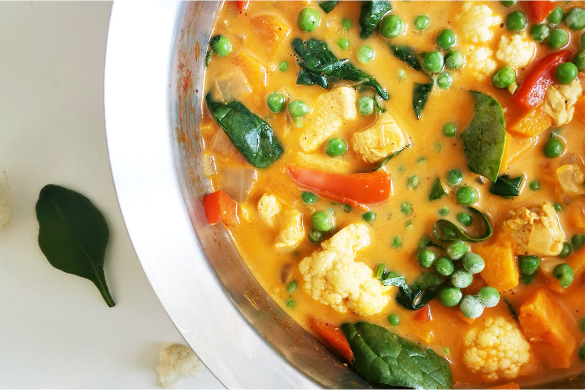 A saucepan of chicken curry with cauliflower, spinach, frozen peas