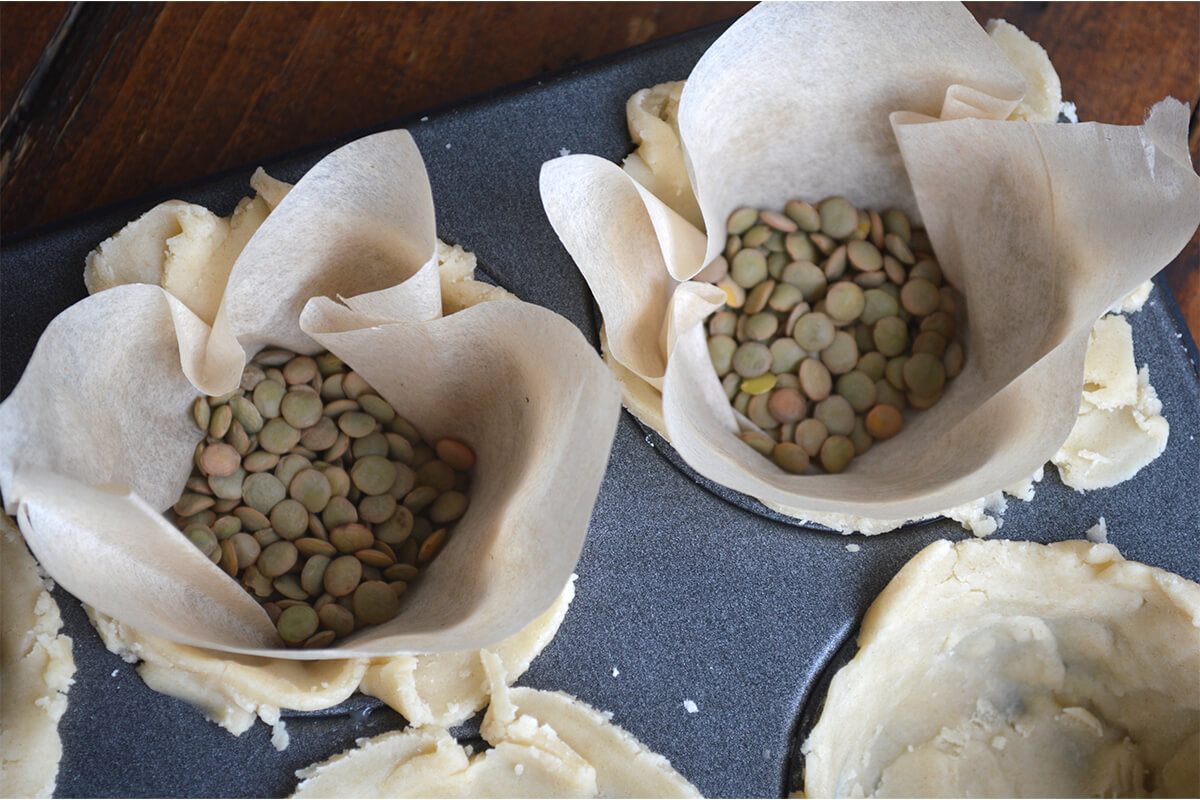 Pastry in cupcake tin lined with baking paper and baking beans