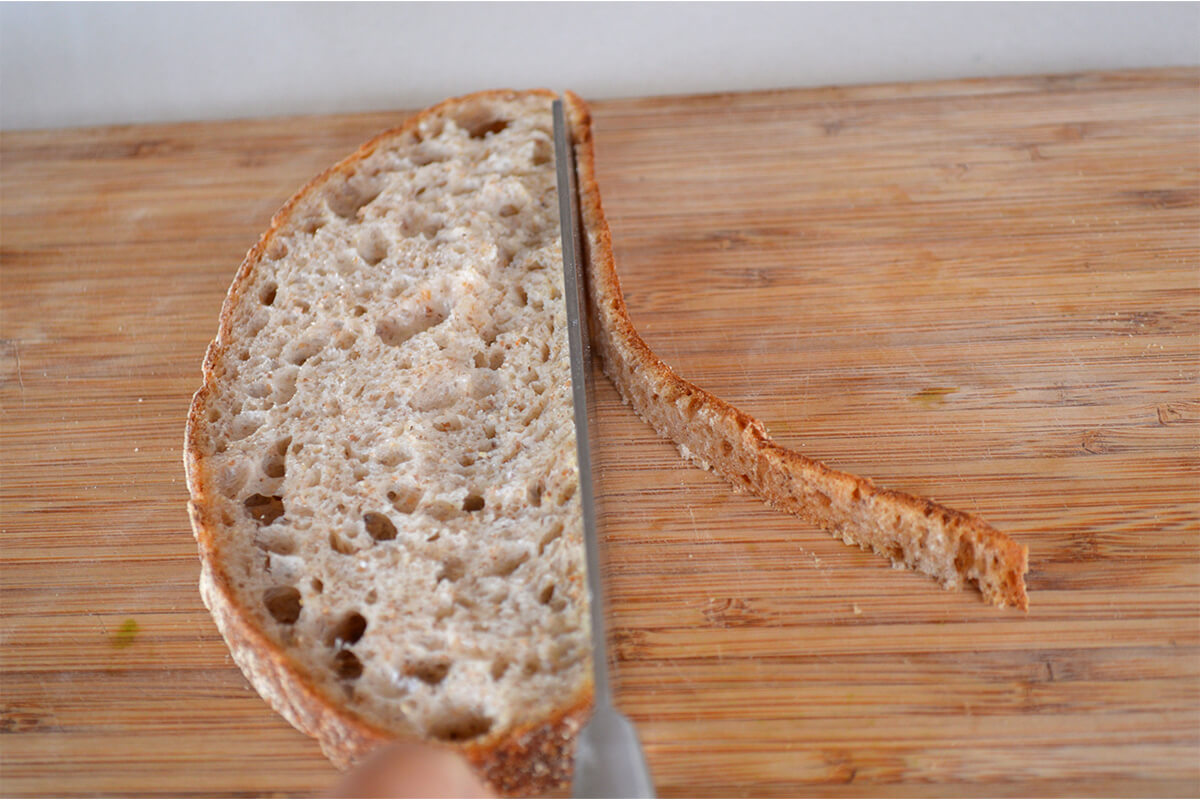 The crust being cut off a slice of bread on a chopping board