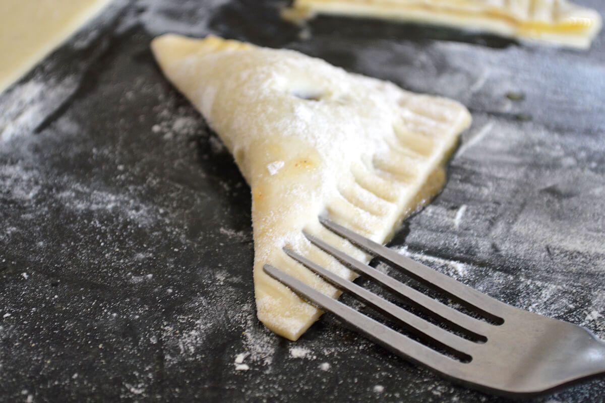 Folded turnover triangles being pressed with the back of a fork