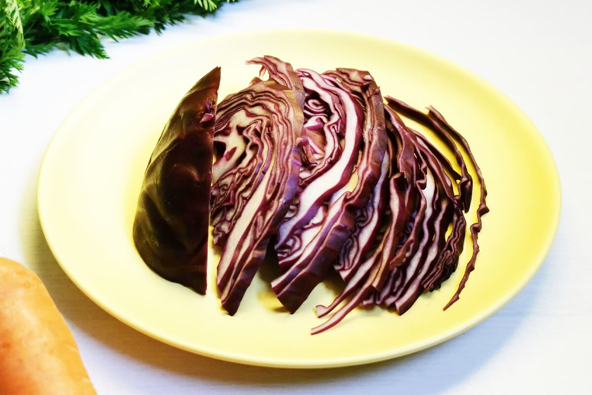 A plate of sliced red cabbage next to some carrots