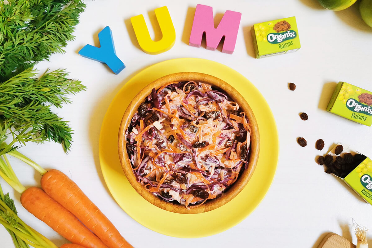 A bowl of apple and red cabbage coleslaw next to some carrots