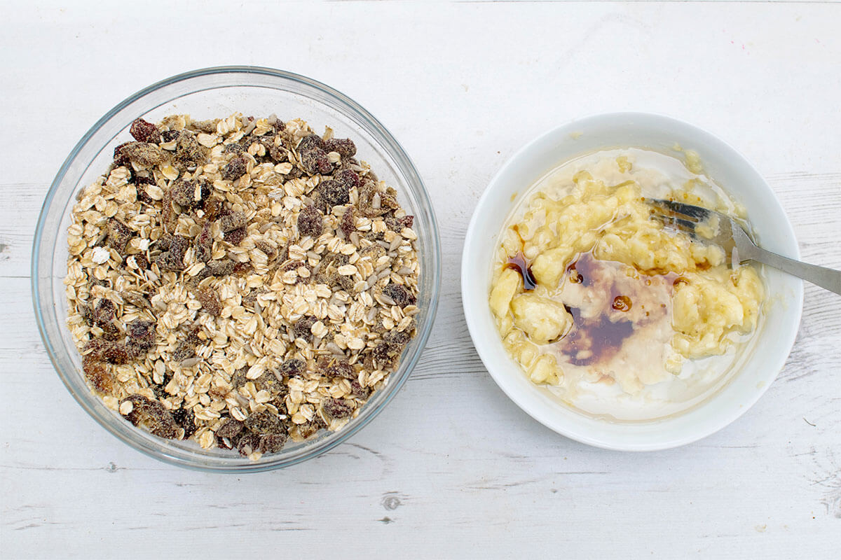 A bowl of oats, flaxseed, sunflower seeds, cinnamon, chopped dates and cranberries next to a bowl of mashed banana with coconut oil, honey and vanilla extract