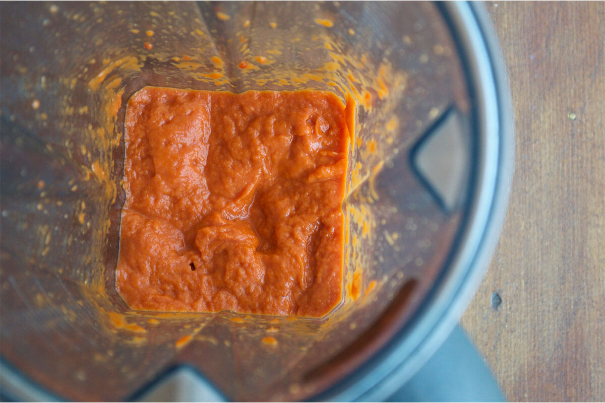 A blender with blended chopped onion, tinned tomatoes and tomato puree