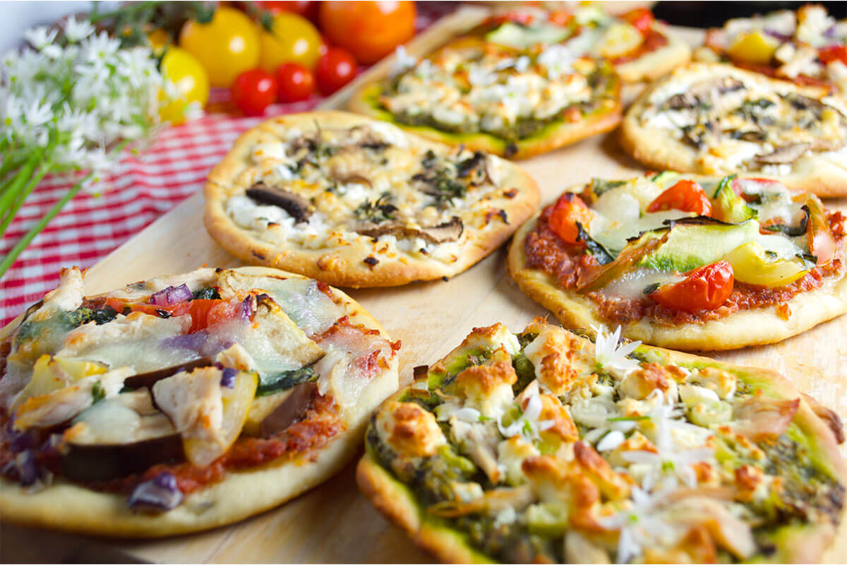 A chopping board with 8 mini pizzas topped with various toppings