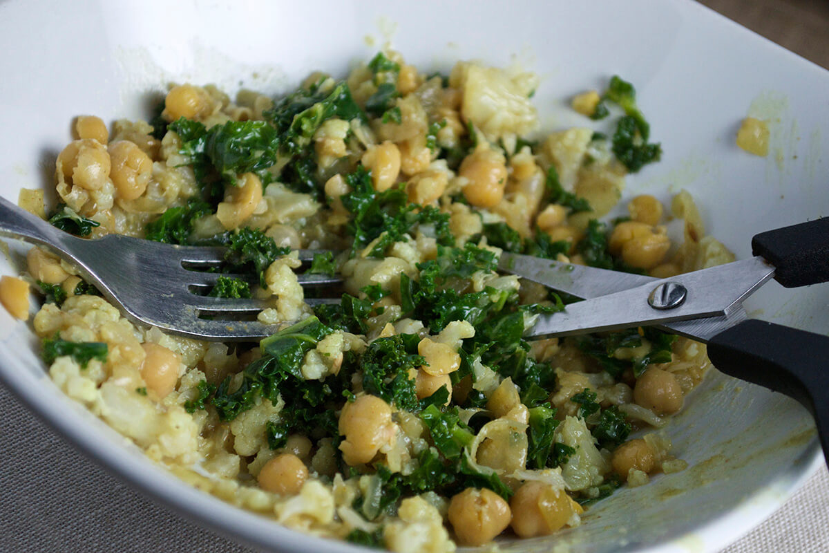 A large bowl of Cauliflower, Chickpea & Kale Baby Curry being cut into smaller pieces with a scissors