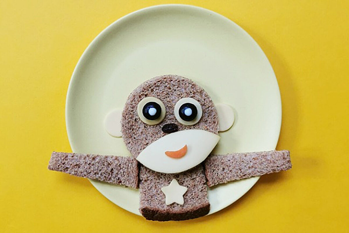 Two finger size slices of bread placed on either side of square to create arms. Slice of carrot placed on semi circle cheese to create a smiling mouth