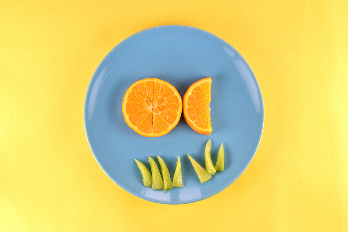 Two semi circle oranges placed on plate and pushed together to create a circle. Third semi circle placed on plate to create the fish's tail