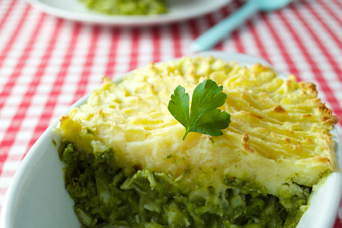 A casserole dish of fish pie with watercress sauce, next to a serving of fish pie