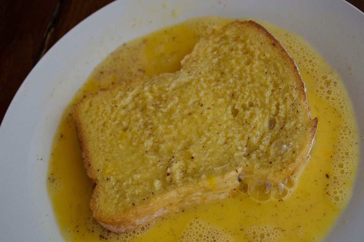 Bread being dipped into and covered by whisked eggs