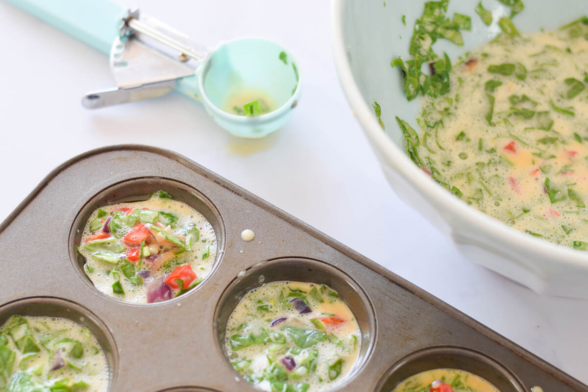 Uncooked Frittata Bites in a muffin tin next to a bowl of the uncooked Frittata Bites mixture