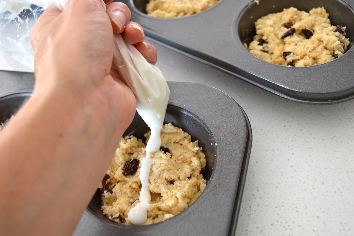 Hot cross muffin mixture in muffin tins with the cross being piped onto them