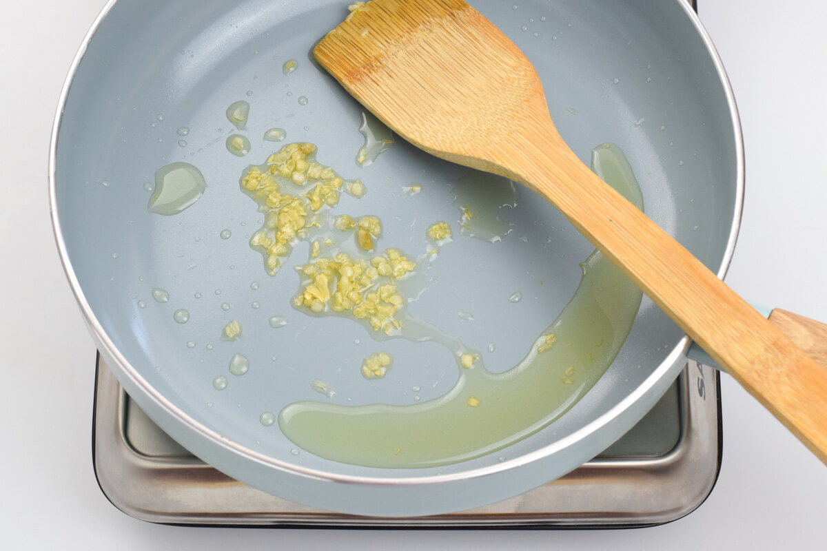 Crushed garlic being softened in a pan with olive oil