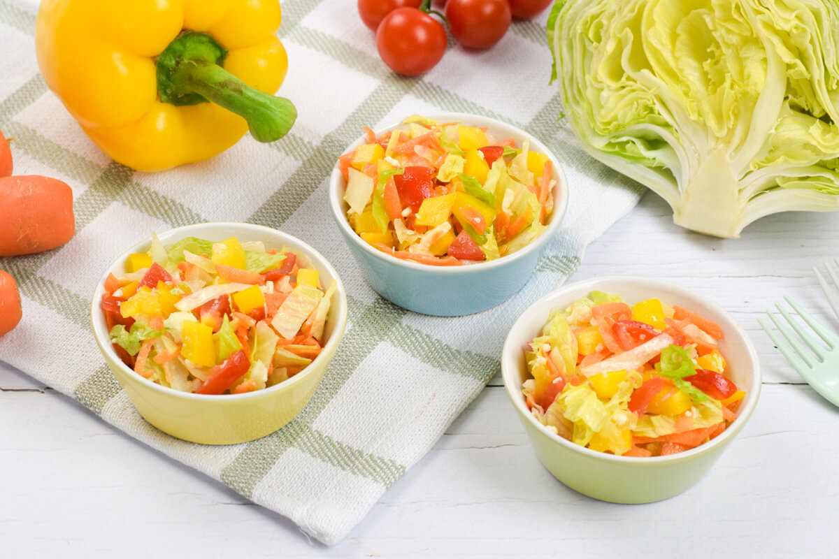 3 small bowls of rainbow salad (lettuce, pepper, carrot, tomato and mozzarella) next to some carrots, lettuce and cherry tomatoes