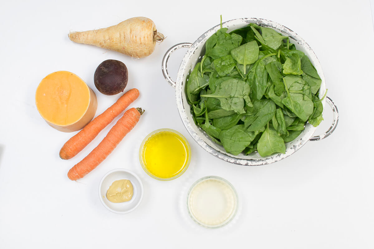 A colander of spinach next to 2 carrots, a parsnip, some butternut squash, beetroot, vegetable oil, olive oil and Dijon mustard