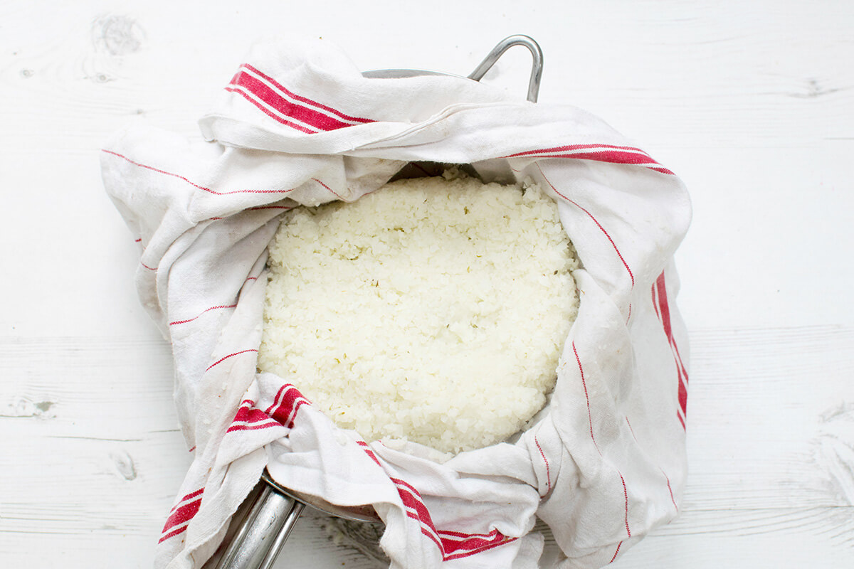 Cauliflower rice being strained with a tea towel 