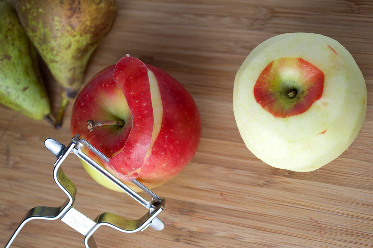 An apple being peeled next to a peeled apple and two whole pears