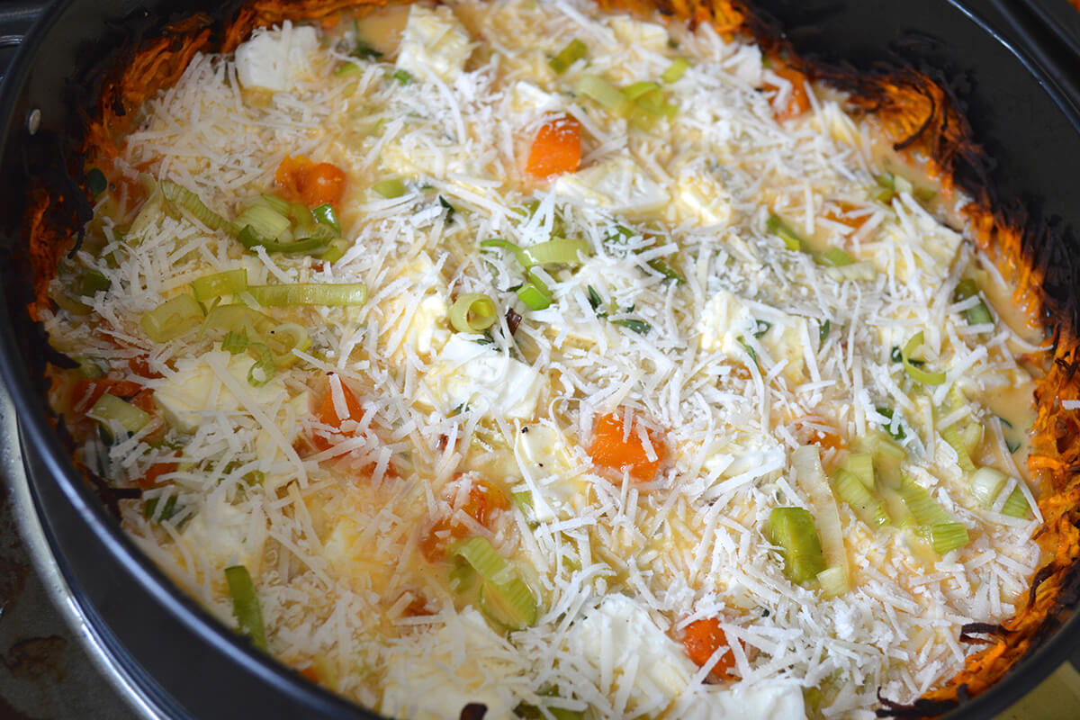 A tart tin with cooked sweet potato crust and uncooked filling in it