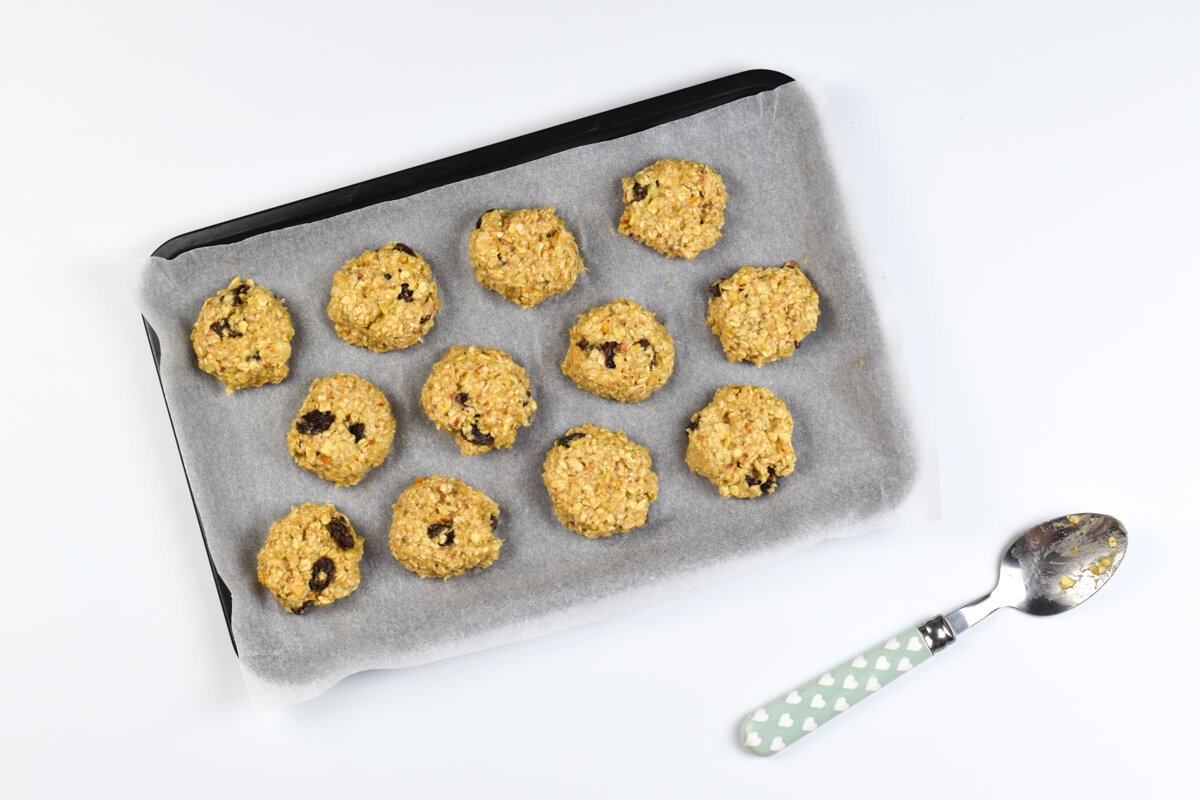 A lined baking tray with 12 uncooked peanut butter raisin cookies on it