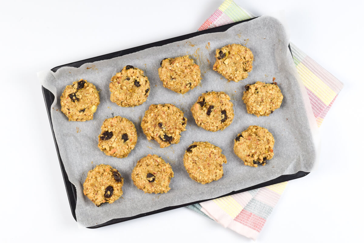 A lined baking tray with 12 peanut butter raisin cookies on it